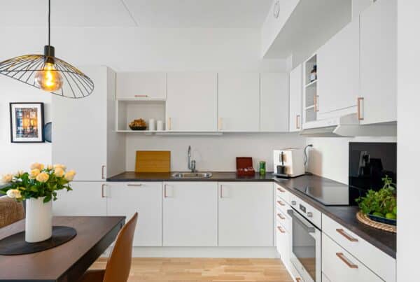 Clean and bright Scandinavian kitchen with white cabinetry, black tile backsplash, butcher block countertops, and sleek under-cabinet knife storage.