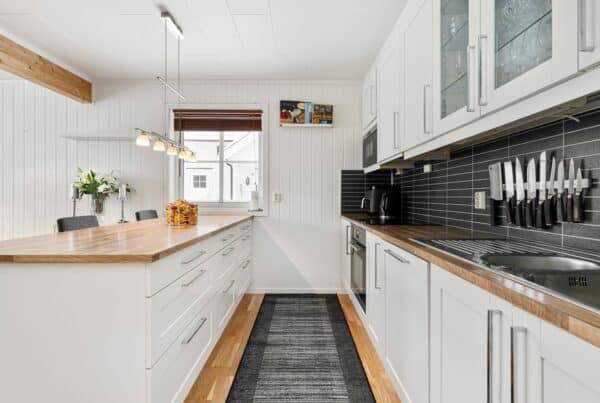 Modern galley-style kitchen with white cabinets, wood countertops, black tile backsplash, and stainless steel sink—designed for both style and functionality.